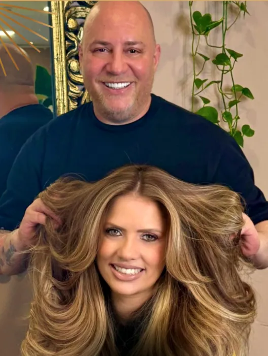 Fabio Alvez sorrindo atrás de uma cliente, segurando o cabelo loiro e volumoso dela